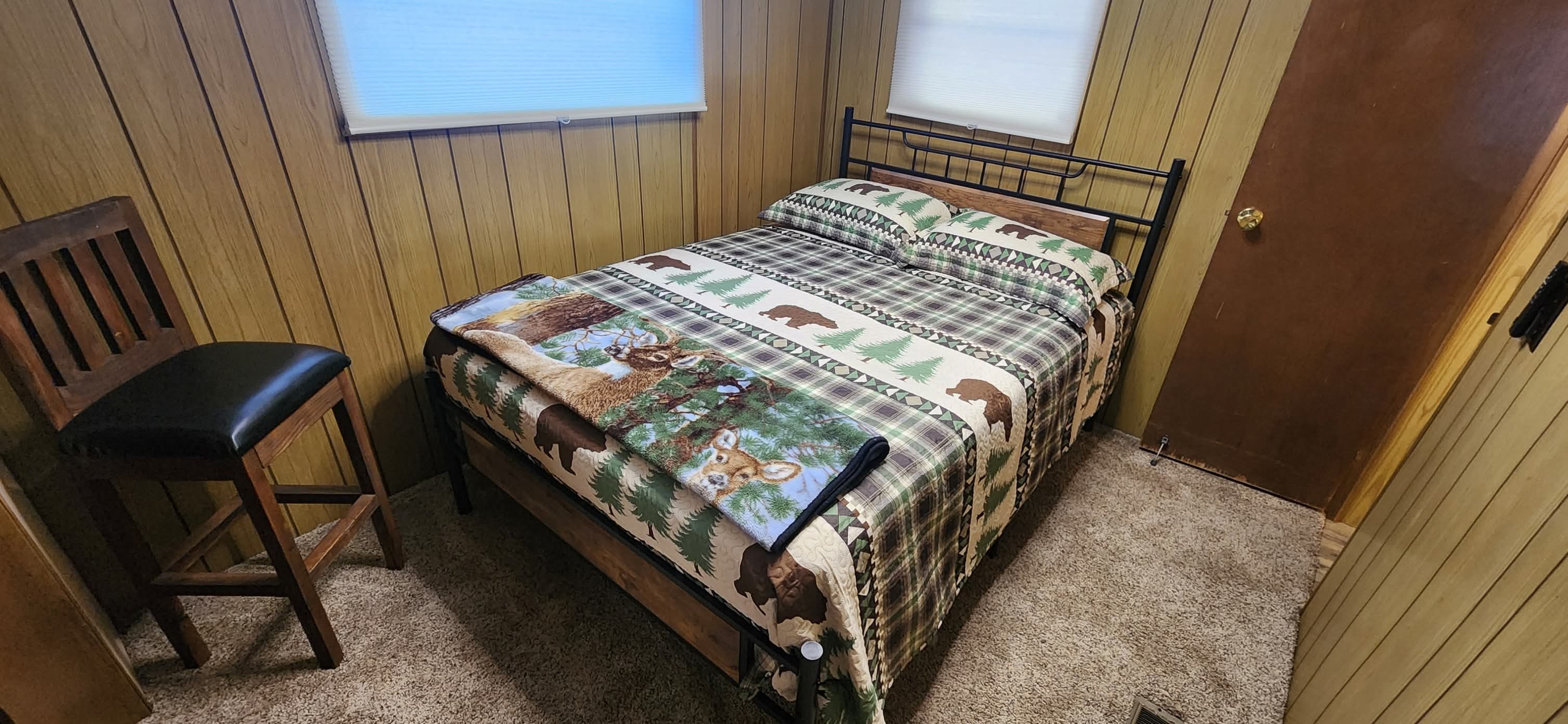 Peaceful bedroom showcasing a full bed with cozy linens, warm ambient lighting from a bedside lamp, natural wood wall paneling, and rustic charm throughout, conveying comfort and tranquility